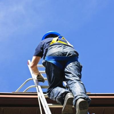 Man-in-safety-harness-climbing-a-ladder-to-get-on-the-roof