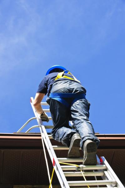 Man-in-safety-harness-climbing-a-ladder-to-get-on-the-roof