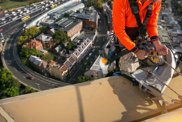 Working caring for commercial roof using abseiling equipment.