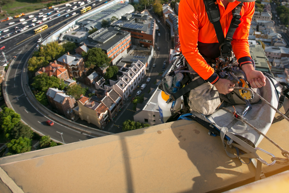 Working caring for commercial roof using abseiling equipment.